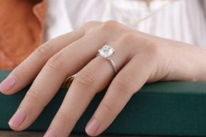 Hand med diamantring på finger, vilar på en mörkgrön bok.